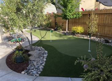 Backyard artificial putting green installed by brown fence